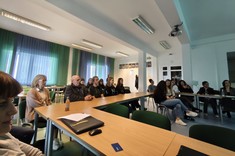 W lekko przyciemnionym pomieszczeniu za stołami ułożonymi w kształcie litery C siedzą słuchacze seminarium. 