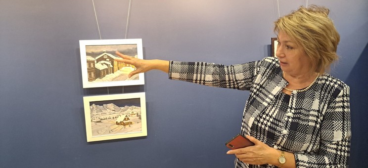 Pani Profesor Galina Kalda opowiada o swoich obrazach. Stoi na tle niebieskiej ściany z wyciągniętą ręką, fot. dr inż. arch. Joanna Dudek