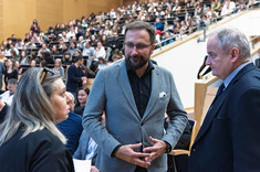 Trzy osoby, kobieta i dwóch mężczyzn, stoją zwrócone do siebie podczas rozmowy. W tle uczestnicy wykładu. Od lewej: prof. arch. A. Sikora, dr. A. Truszczyński, prof. L. Lichołai.