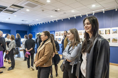 Zdjęcie grupy osób na tle wystawy. Na pierwszym planie trzy młode kobiety, uśmiechają się. Na zdjęciu na pierwszym planie studentki kierunku architektura.