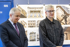 Aleksander Busz przemawia do obecnych na wernisażu, w tle zdjęcia z wystawy, obok przemawiającego stopi i słucha Dziekan Lech Lichołai