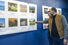 Dwóch mężczyzn z ciemnymi włosami i brodami przygląda się wystawie. Jeden z nich wskazuje jedno ze zdjęć ręką. Na zdjęciu od prawej: arc. Ł Bajda, arch. J. Dudek.