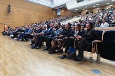 Zdjęcie sali wykładowej w całości wypełnionej słuchaczami. Miejsca siedzące są ustawione w równoległych rzędach, które stopniowo wznoszą się ku tyłowi pomieszczenia.