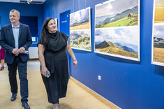 Mężczyzna i kobieta ubrani na ciemno idą wzdłuż ściany z zawieszonymi planszami, przyglądają się prezentowanym fotografiom.