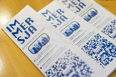 Trzy ulotki koła naukowego „Immesja. Dostępna Rzeczywistość” leżą na drewnianym stole, fot. Beata Motyka