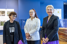 Trzy kobiety uśmiechają się do zdjęcia. W tle ciemno niebieska ściana i plansze ze zdjęciami. Na zdjęciu od lewej: dr arch. K. Kozłowska, mgr J. Makar-Płaza, prof. M. Kłos.