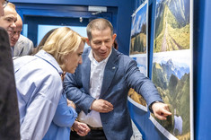 Mężczyzna, autor wystawy, stoi przy jednej z plansz i wskazuje ręką fragment zdjęcia, tłumaczy coś kilku osobom stojącym obok. 