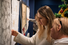 Rozmowa dwóch kobiet przy hafcie powieszonym na ścianie