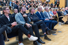 Duża grupa osób siedzących w rzędach podczas wykładu. Na pierwszym planie grupa pięciu mężczyzn. Na pierwszym planie od prawej: D. Urbanik, prez. K. Fijołek, prof. arch. W. Maas, dr. A. Truszczyński.