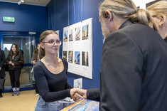 Mężczyzna ustawiony plecami do zdjęcia wręcza nagrodę młodej kobiecie. W tle plansze ze zdjęciami. Na zdjęciu: stud. arch. Z. Dąbrowska i arch. W. Matłok.