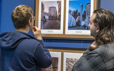 Dwóch mężczyzn ogląda dwie fotografie wiszące na niebieskiej ścianie