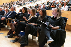 Duża grupa osób siedzących w rzędach podczas wykładu. Na pierwszym planie cztery kobiety ubrane na czarno. Na pierwszym planie od prawej: prof. arch. A. Sikora, arch. A. Pomykała, arch. D. Bober, arch. A. Jóźwiakowska.