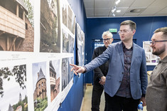 Damian Pękalski wskazuje z zainteresowaniem na jedną z prezentowanych fotografii, obok niego stoją Aleksander Busz i Przemysław Gąsiorski