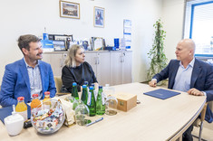 Trzy osoby dwóch mężczyzn i kobieta po środku siedzą przy stole podczas spokojnej rozmowy. Uśmiechają się. 