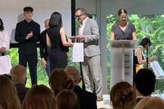 Na pierwszym planie zdjęcia widać jak na scenie wręczany jest dyplom Pani Reginie Otto przez członka Jury konkursu „Dyplom Roku SARP im. Zbyszka Zawistowskiego 2025”