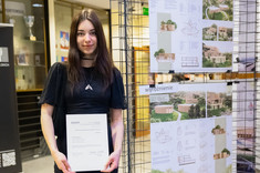 Na zdjęciu laureatka konkursu trzymająca w dłoniach dyplom i nagrodę. Kobieta stoi obok swojej pracy konkursowej zawieszonej na metalowych siatkach, fot. Dawid Zientek