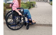 Osoba na wózku inwalidzkim stoi przed krawężnikiem chodnika