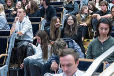 Zbliżenie na słuchaczy wykładu siedzących na schodach.