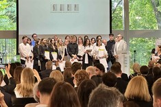 Na pierwszym planie zdjęcia widać osoby które stoją frontem do stojących na scenie finalistów konkursu