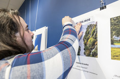 Mężczyzna z długimi włosami wiesza na planszy opis do zdjęcia.