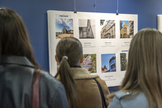 Uczestnicy wystawy przyglądaj się planszy ze zdjęciami. Zdjęcie zrobione od tyłu.