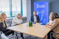 Osoby zgromadzone podczas podpisania umowy podczas swobodnej rozmowy. Pięć osób, cztery kobiety i jeden mężczyzna siedzi wokół stołu na tle przeszklonej ściany. 