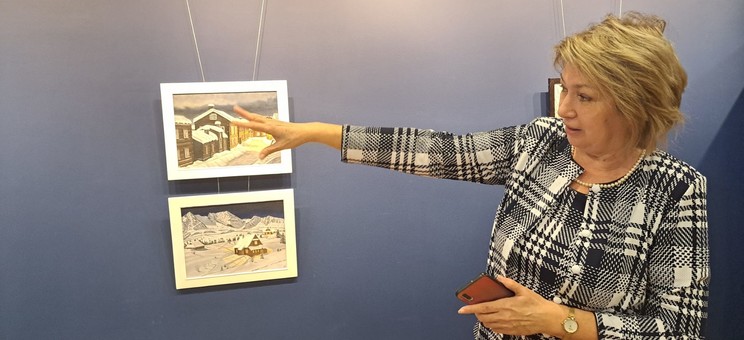 Pani Profesor Galina Kalda opowiada o swoich obrazach. Stoi na tle niebieskiej ściany z wyciągniętą ręką, fot. dr inż. arch. Joanna Dudek