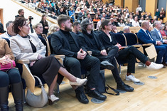 Duża grupa osób siedzących w rzędach podczas wykładu. Na pierwszym planie, pośrodku, trzech mężczyzn ubranych na czarno. Na pierwszym planie architekci z grupy TKHolding.