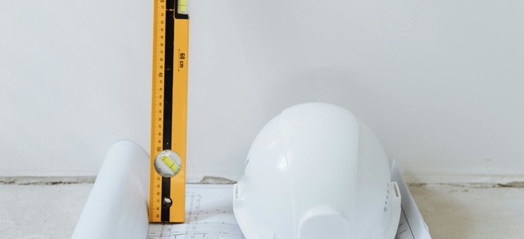 Kask budowlany, plan i poziomica symbolizują trwający remont
