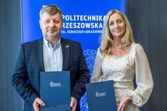Od lewej rektor, prof. P. Koszelnik, dr. B. Szafrańska. Dwie osoby, kobieta i mężczyzna stoją obok siebie, delikatnie się uśmiechają. Oboje prezentują podpisane umowy.  W tle niebieski baner z białym napisem Politechnika Rzeszowska.
