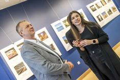 Na pierwszym palnie mężczyzna w jasnej marynarce i kobieta ubrana na czarno uśmiechają się do zdjęcia. W tle plansze ze zdjęciami. Na zdjęciu: prof. P. Nazarko, arch. A. Pomykała.