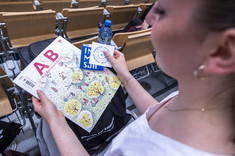 Studentaka prezentująca najnowszy numer czasopisma Architektura i Biznes oraz naklejki koła naukowego Immersja.