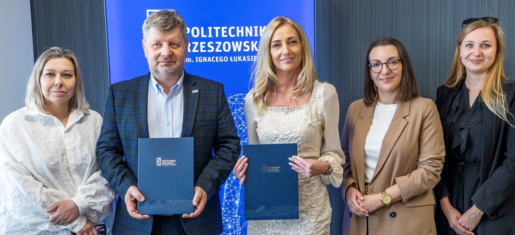 Od lewej prof. A. Sikora, rektor, prof., P. Koszelnik, dr. B. Szafrańska, p. P. Multan, arch. D. Bober. Na zdjęciu na tle ciemnej ściany z wyróżniającym się niebieskim banerem z białym napisem Politechnika Rzeszowska stoi pięć elegancko ubranych osób. Dwie pośrodku trzymają okładki z umowami.