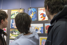Trzej mężczyźni podziwiający zawieszone na ścianie prace studentów kierunku "Inżynieria wzornictwa przemysłowego"