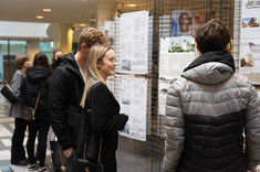 Na zdjęciu grupa rozmawiających ze sobą studentów. W tle stoi wystawa prac konkursowych: prostokątne plansze zawieszone na metalowych siatkach, fot. Dawid Zientek