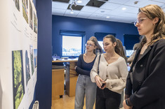 Na pierwszym planie trzy młode kobiety przyglądają się białej planszy z kolorowymi zdjęciami. Na zdjęciu: studentki kierunku architektura.